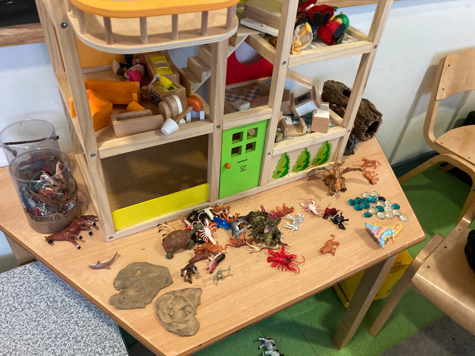 Small figures, animals and treasures laid out beside a wooden dolls' house